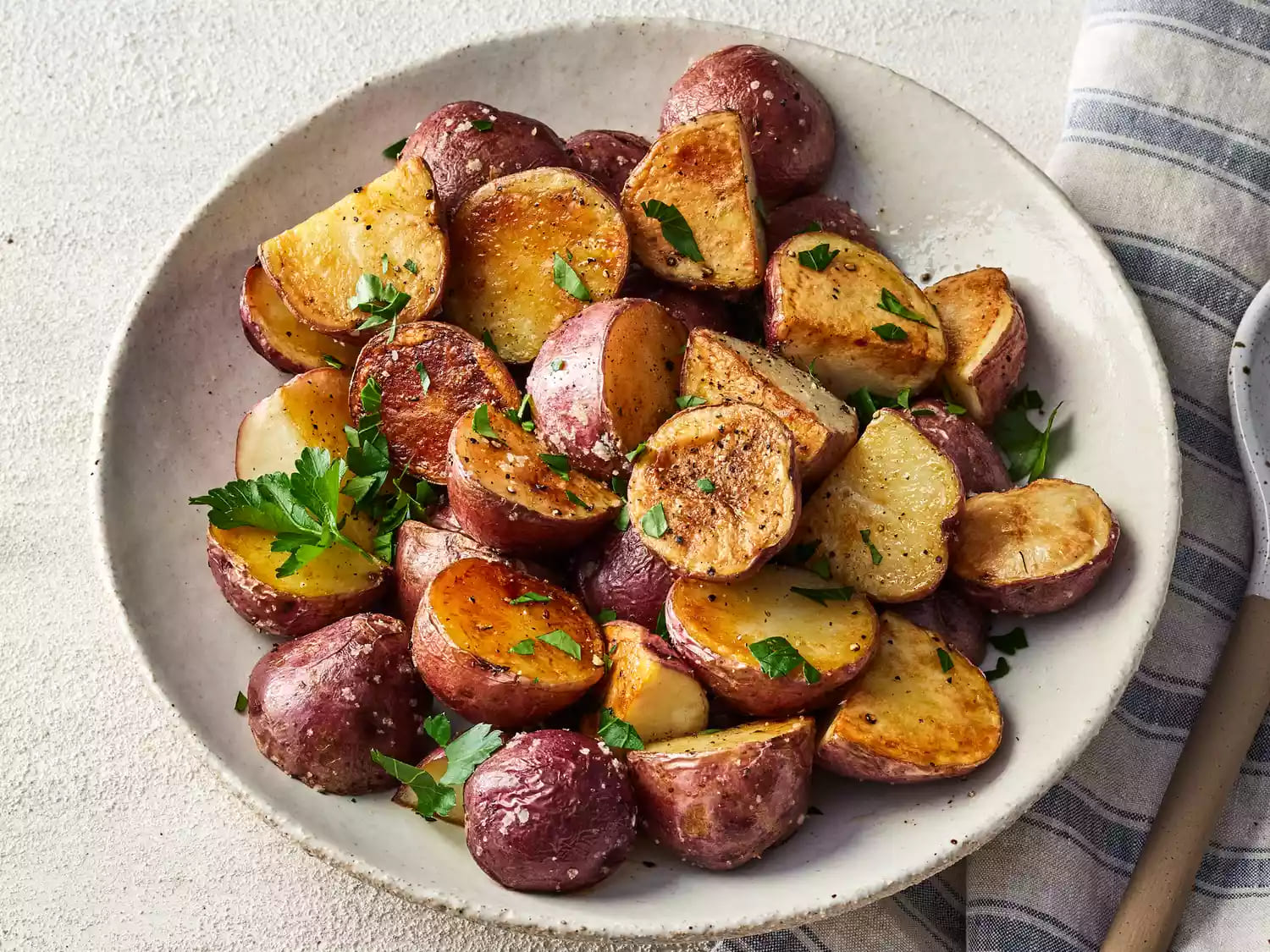 A bowl of roasted new red potatoes garnished with parsley