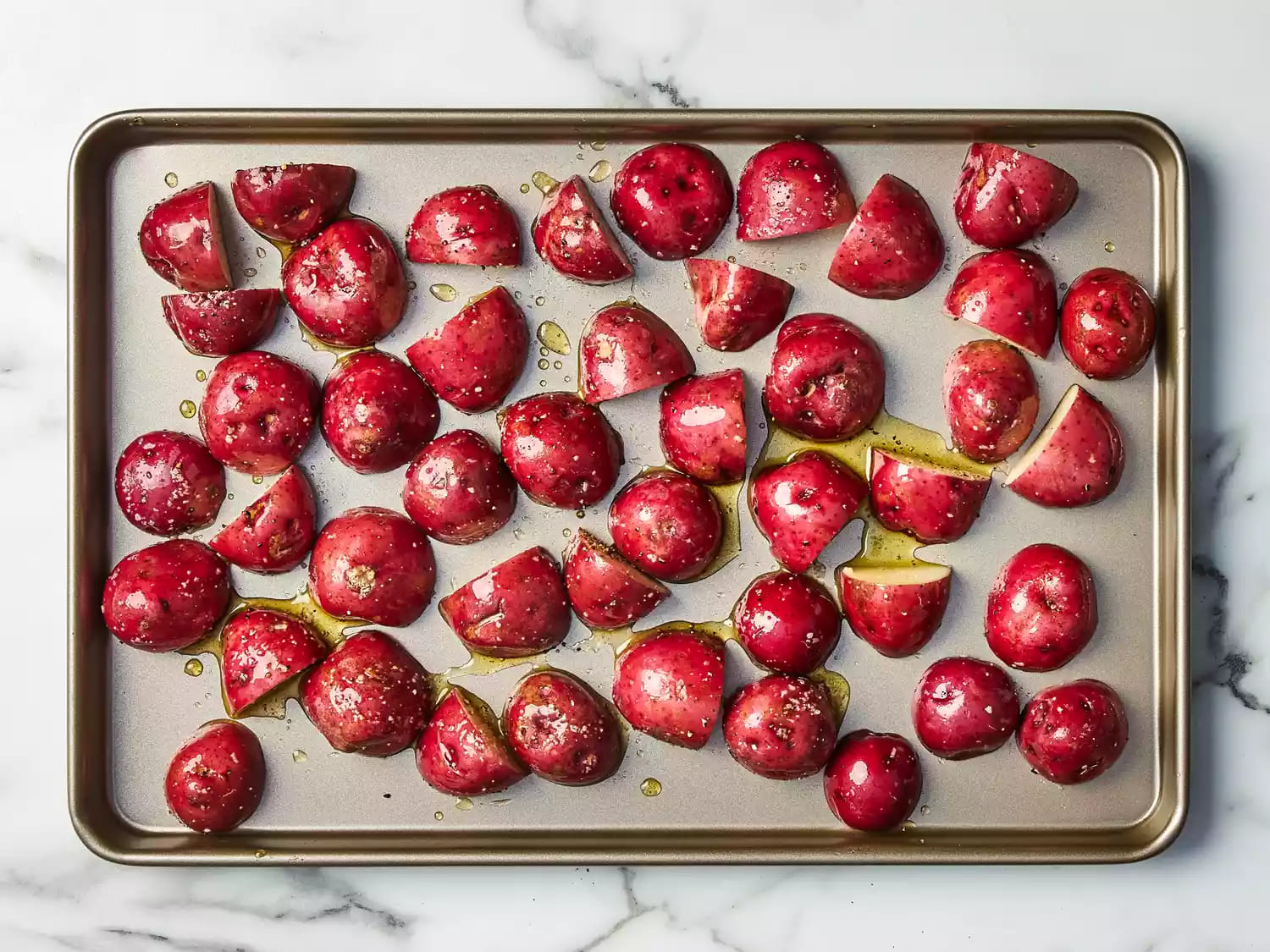 Seasoned red potatoes arranged cut-side down on a baking sheet