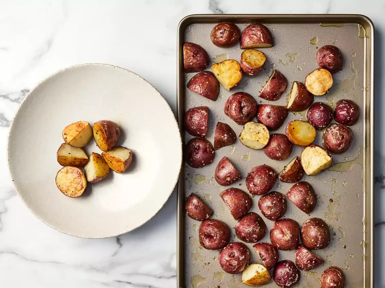 Golden roasted red potatoes on a baking sheet, partially plated